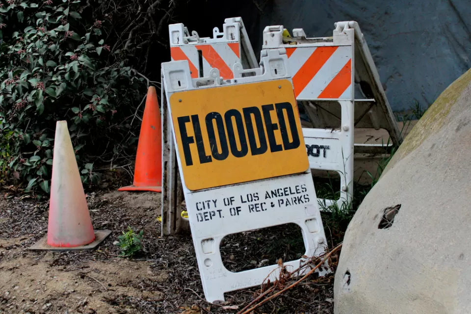 Sandwich sign with "Flooded" and "CIty of Los Angeles Dept of Rec and Parks" sits in ground near orange traffic cone
